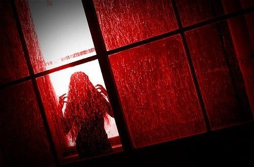 A shadowy figure stands behind a red-tinted window