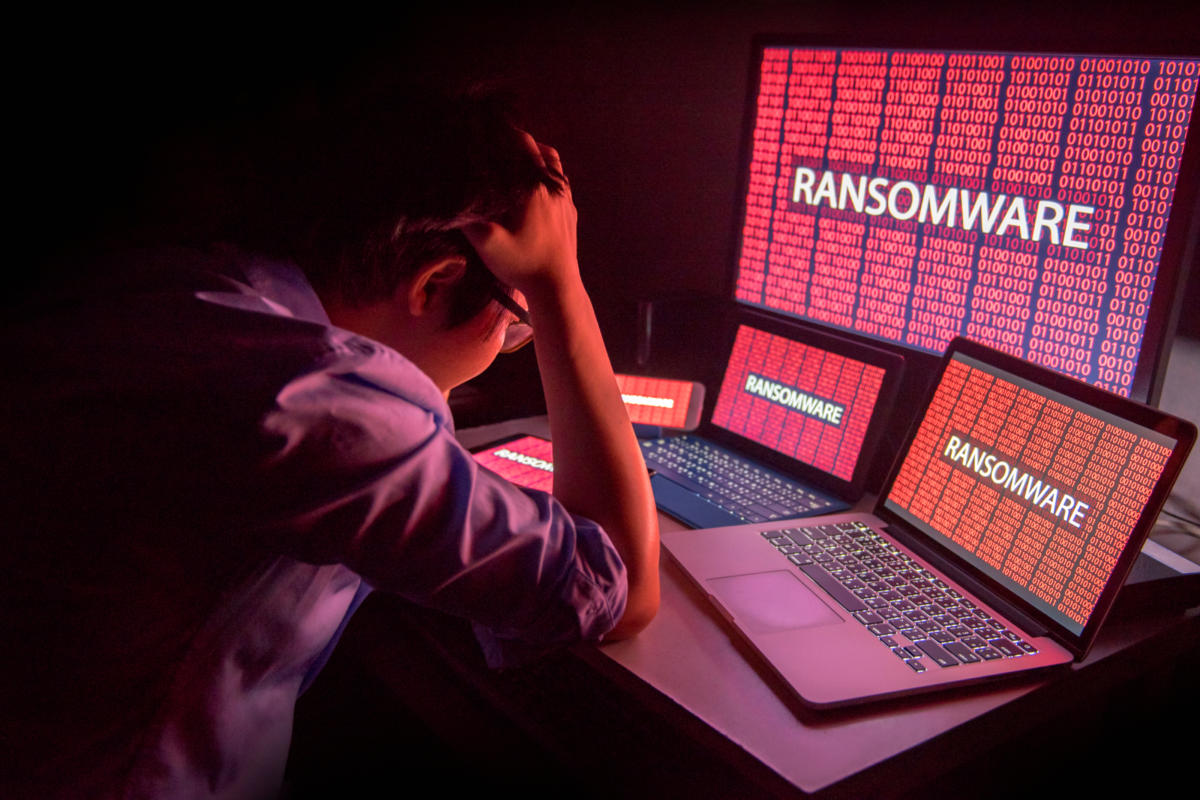 Person visibly distressed by multiple computer screens displaying the word "RANSOMWARE"