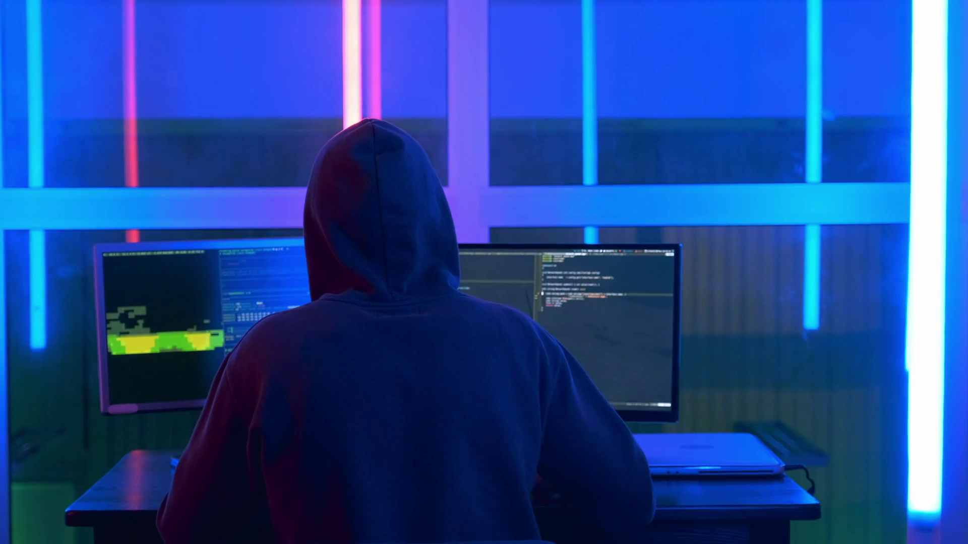 Person in a dark hoodie sitting in front of multiple computer screens